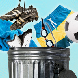 Cropped image of the top half of a trash can, against a blue background. Several objects are being tossed into the can, including a beach towel, shin guards, soccer cleats, swim goggles, swim trunks, and a soccer ball.